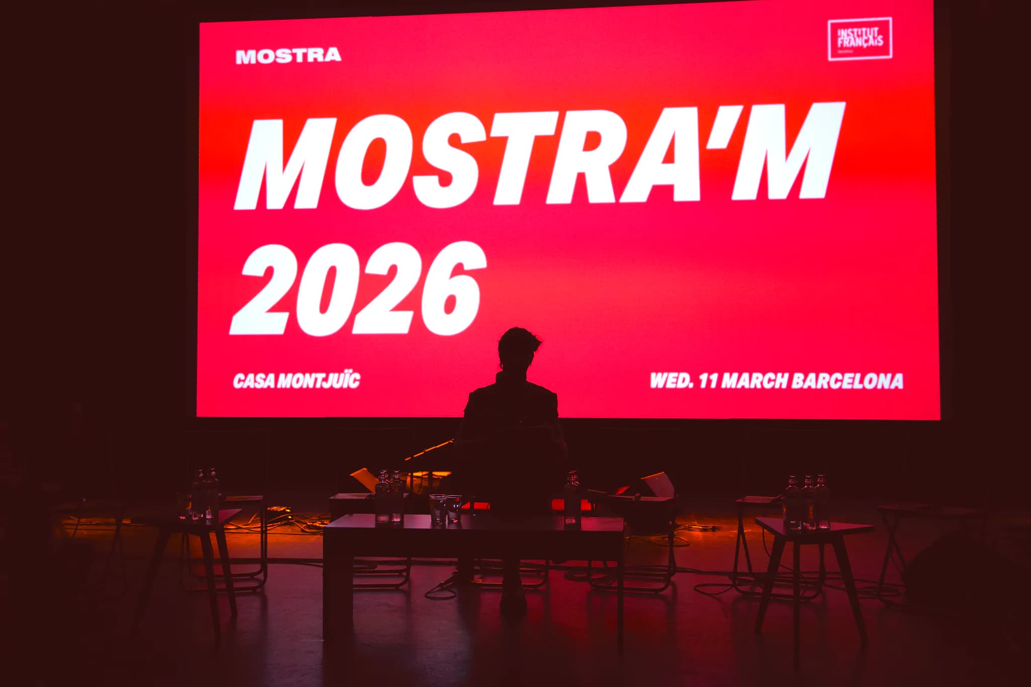 Obertura de Mostra'm 2026 a Casa Montjuïc: un ponent a l'escenari davant la pantalla vermella